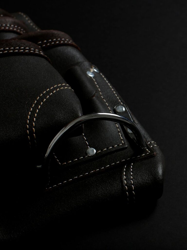 Dark leather bag with rolled handles, contrast stitching, rivet studs and a metal ring