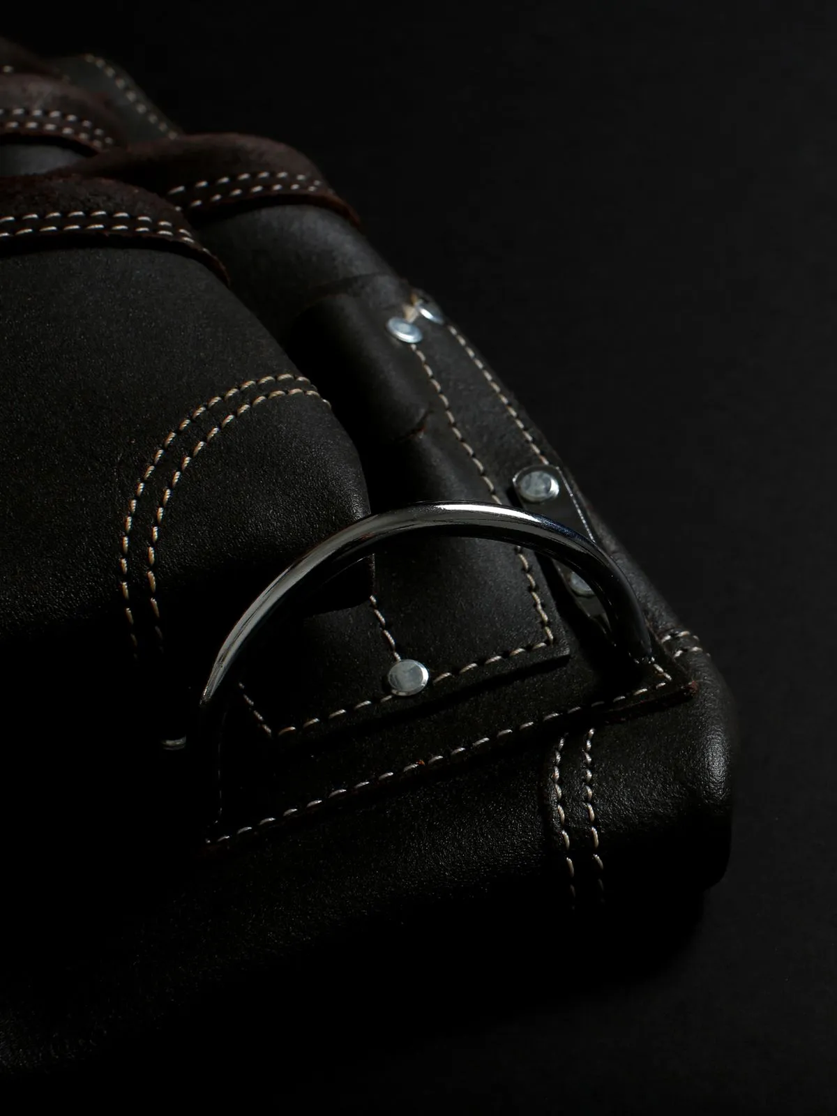 Dark leather bag with rolled handles, contrast stitching, rivet studs and a metal ring