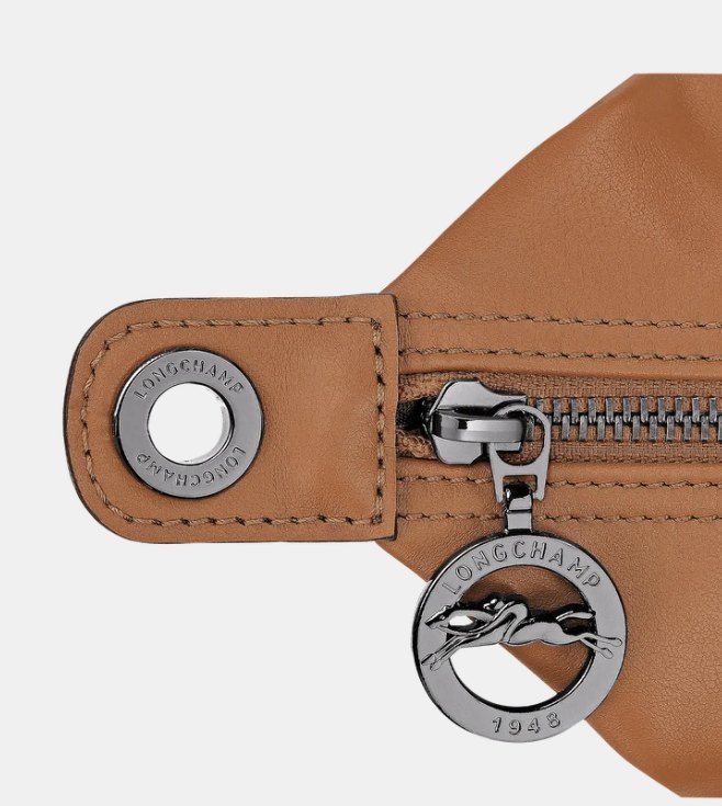 Close-up of a Longchamp press stud engraved with the brand name and a round zip pull with the galloping horse and the date 1948