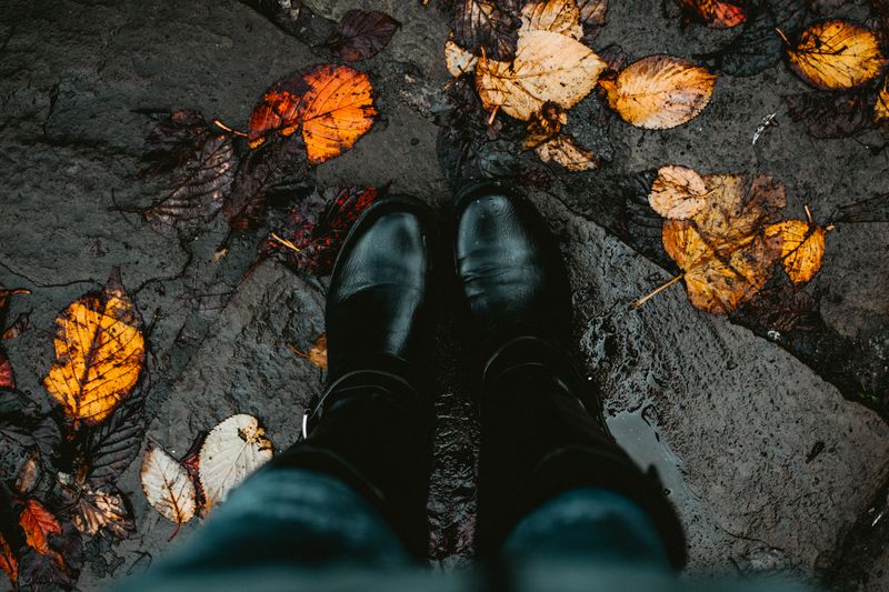 Stivaletti in pelle nera su selciato bagnato con foglie d'autunno