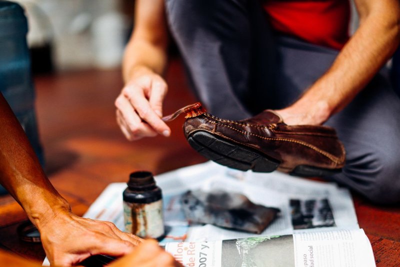 Mani che passano la spazzola con crema nutriente su una scarpa in pelle marrone dopo le macchie di sale