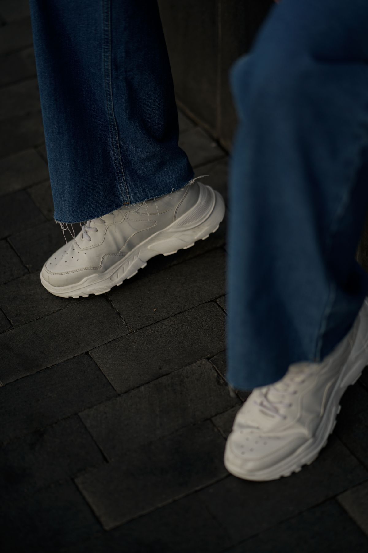White sneakers with scuffed toes and grey midsoles on dark paving, before cleaning