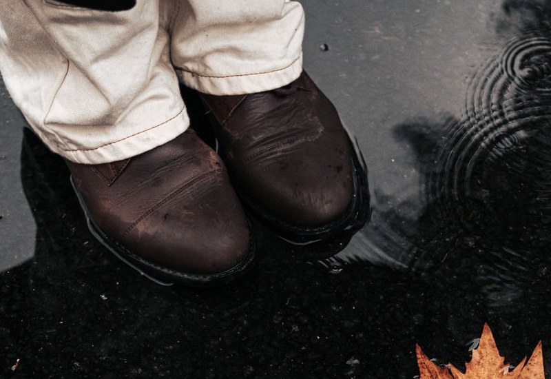 Dark brown leather boots standing in a shallow rain puddle
