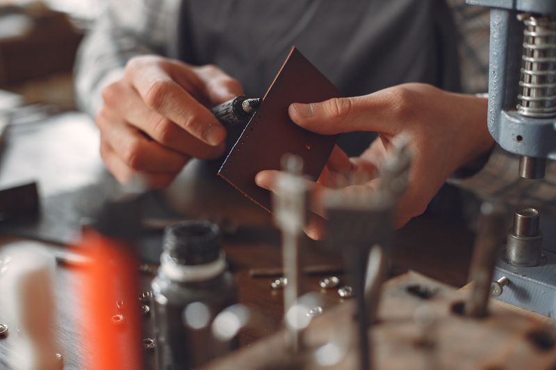 Craftsman finishing the cut edge of a small brown leather panel with a hand tool in a workshop