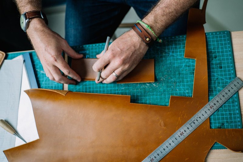 Leather worker cutting hide at a workbench with repair tools