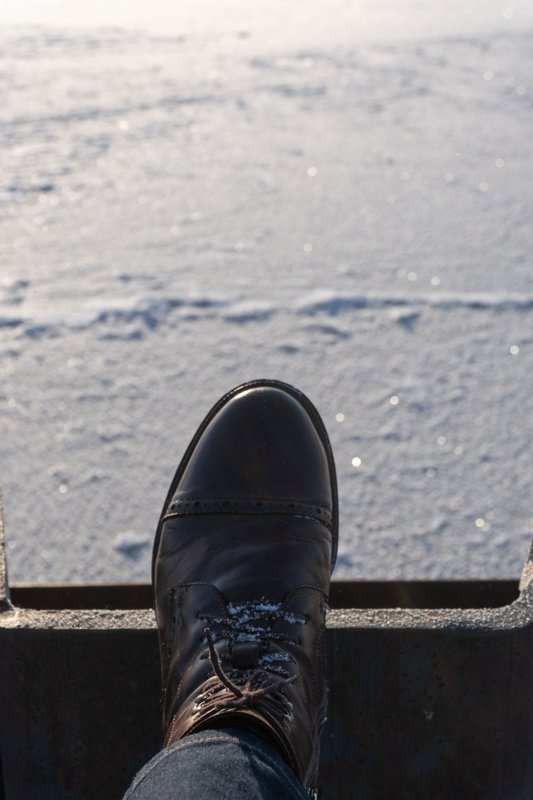 Scarpa in pelle scura con neve fra i lacci, prima del trattamento contro le macchie di sale