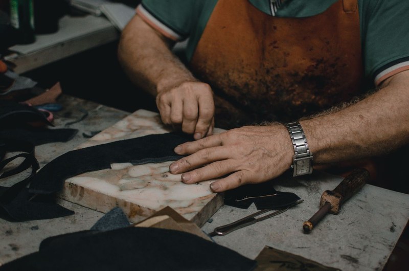Shoemaker cutting and shaping leather at a workshop bench