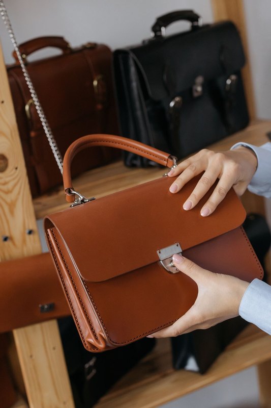 Hands holding a smooth tan leather handbag