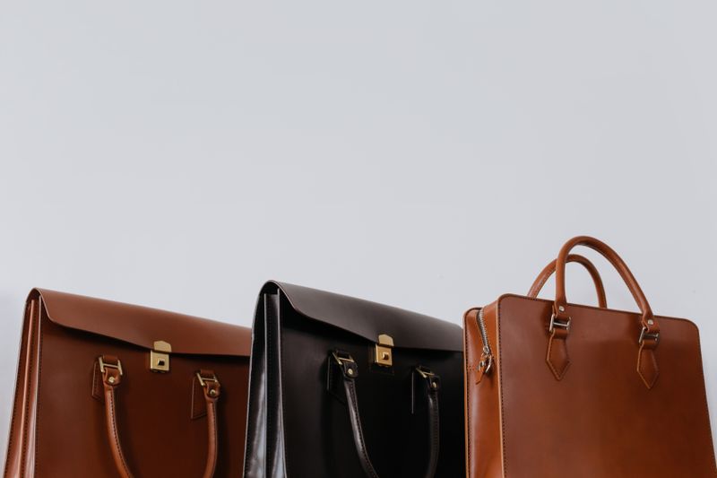 Three structured handbags in tan, dark brown and cognac leather with plain metal hardware and no visible branding